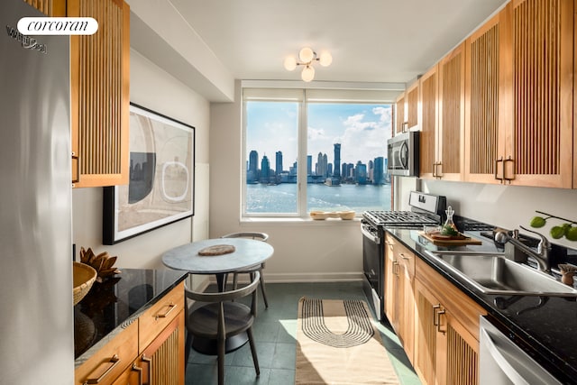 kitchen featuring dark tile patterned flooring, dark stone countertops, a view of city, stainless steel appliances, and a sink