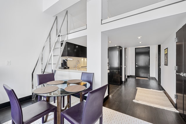 dining area featuring dark wood-type flooring, a high ceiling, and baseboards