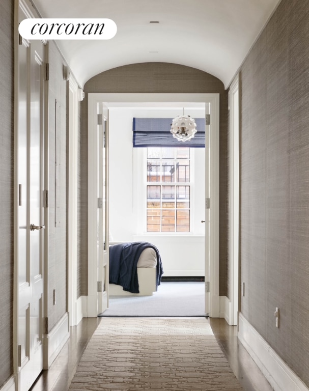 hallway with lofted ceiling, an inviting chandelier, and baseboards