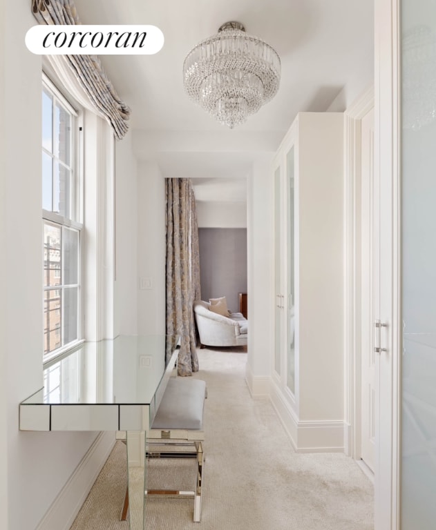 hall with baseboards, a chandelier, and light colored carpet