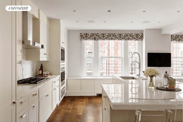 kitchen with light stone counters, white cabinets, appliances with stainless steel finishes, wall chimney range hood, and dark wood finished floors