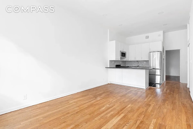 kitchen featuring light wood finished floors, a peninsula, appliances with stainless steel finishes, dark countertops, and tasteful backsplash