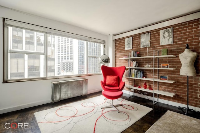 sitting room featuring radiator heating unit, dark hardwood / wood-style floors, and brick wall