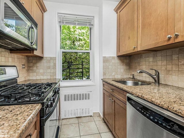 kitchen featuring light stone counters, light tile patterned flooring, a sink, appliances with stainless steel finishes, and radiator