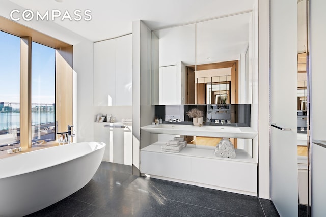 full bathroom featuring a soaking tub, granite finish floor, and vanity