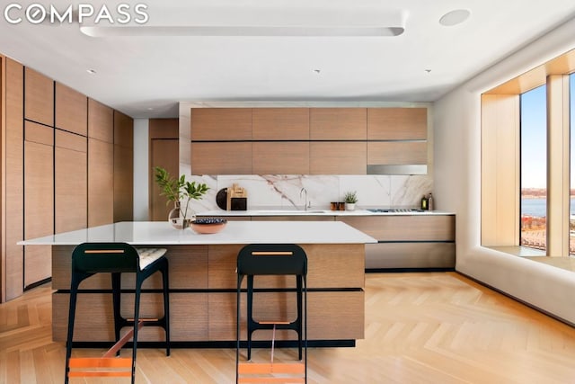 kitchen with light parquet flooring, a kitchen island with sink, a breakfast bar area, and decorative backsplash