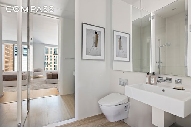 ensuite bathroom with connected bathroom, a sink, toilet, wood finished floors, and a shower