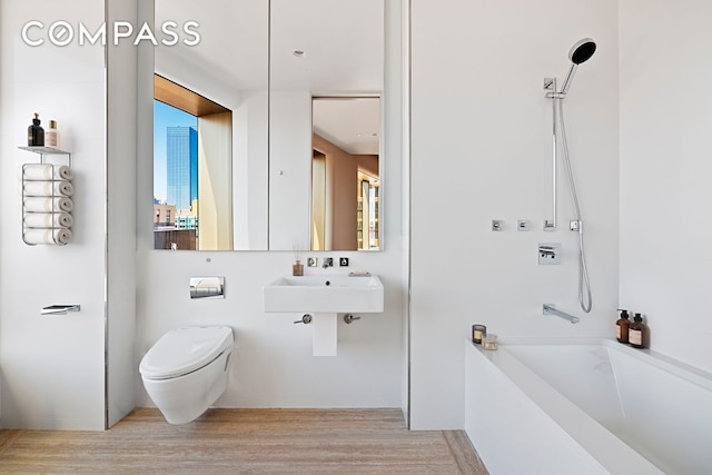 bathroom featuring toilet, a sink,  shower combination, and wood finished floors