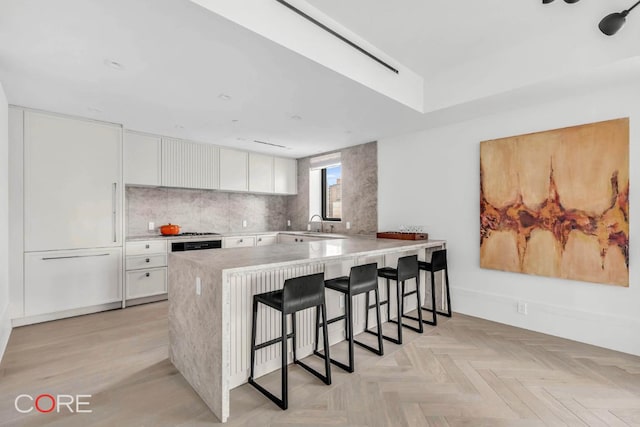 kitchen featuring a breakfast bar area, light parquet floors, white cabinets, decorative backsplash, and kitchen peninsula