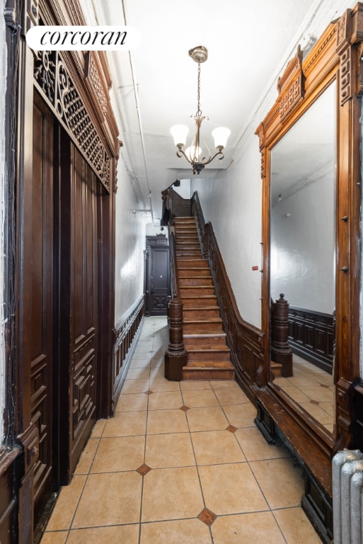 staircase featuring tile patterned flooring, radiator, crown molding, and a chandelier