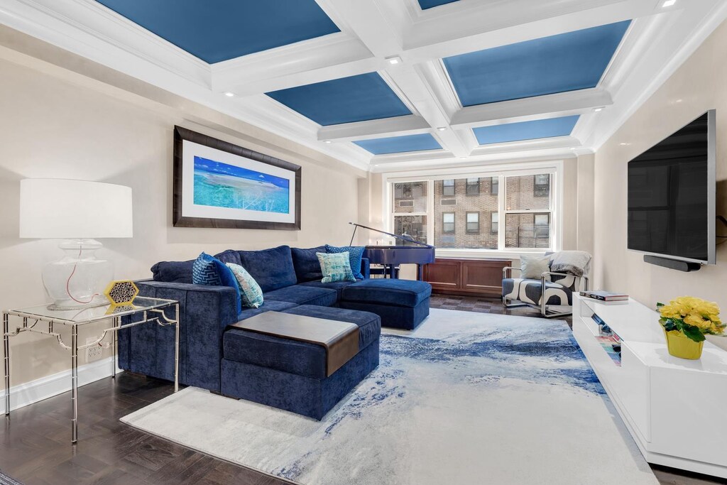 living room featuring wood finished floors, baseboards, coffered ceiling, beam ceiling, and crown molding
