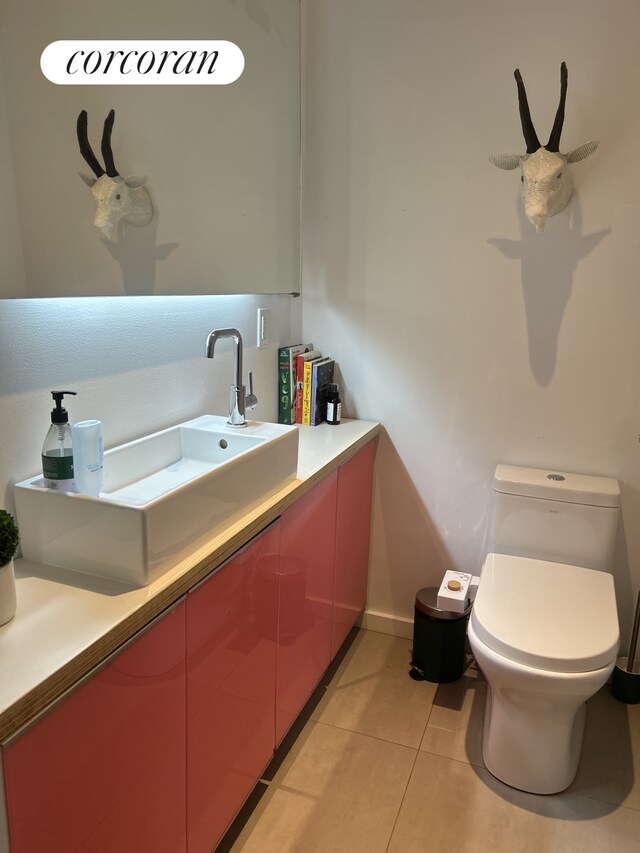 half bathroom with vanity, tile patterned floors, toilet, and baseboards