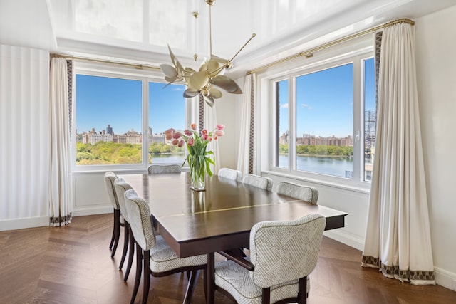 dining area featuring dark parquet flooring, a chandelier, and a water view