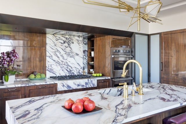 kitchen featuring a sink, appliances with stainless steel finishes, light stone countertops, open shelves, and an inviting chandelier