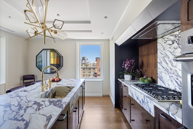 1049 5th Ave Unit 19B, New York City, NY 10028 - kitchen with stainless steel gas stovetop, wood finished floors, a chandelier, light stone counters, and dark brown cabinetry