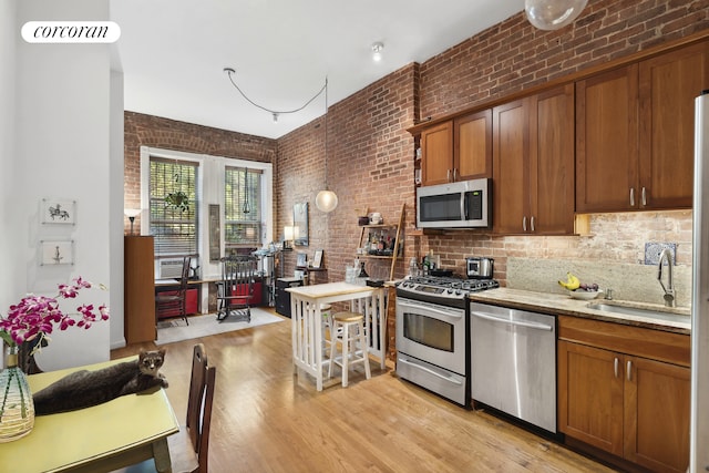 kitchen featuring brick wall, brown cabinetry, stainless steel appliances, light wood-style floors, and a sink