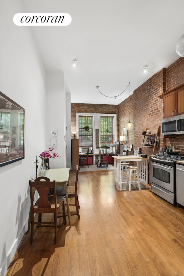 kitchen with brick wall, stainless steel appliances, light wood finished floors, and brown cabinetry
