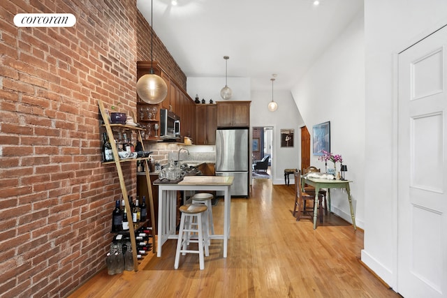 kitchen featuring pendant lighting, appliances with stainless steel finishes, a breakfast bar, light wood-type flooring, and brick wall