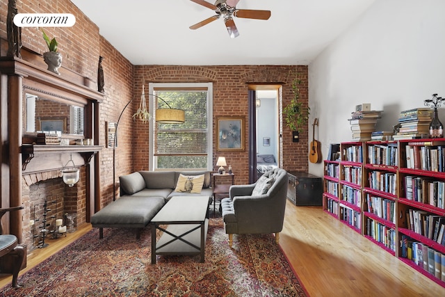 sitting room with wood finished floors, brick wall, a ceiling fan, and a brick fireplace