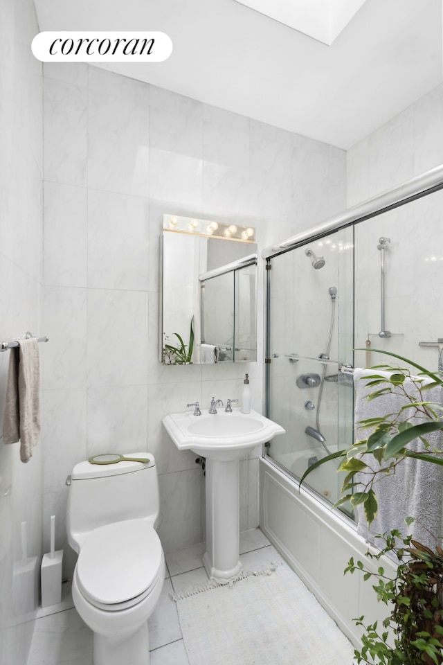full bath with tile walls, tile patterned floors, bath / shower combo with glass door, and toilet