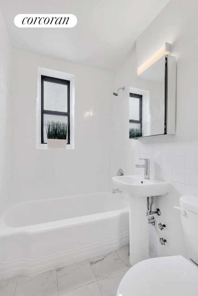 bathroom featuring toilet, tiled shower / bath combo, and tile walls