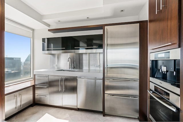 kitchen with a sink, stainless steel appliances, dark brown cabinetry, light countertops, and light tile patterned floors