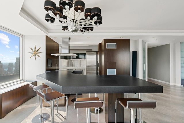 kitchen with a kitchen bar, stainless steel refrigerator, island exhaust hood, dark countertops, and light tile patterned floors