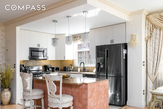 kitchen with appliances with stainless steel finishes, light stone counters, a sink, a breakfast bar area, and white cabinetry