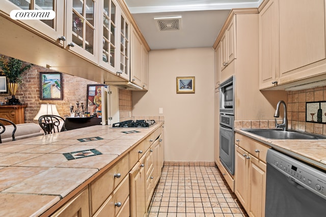 kitchen featuring tile countertops, gas cooktop, brick wall, dishwasher, and sink