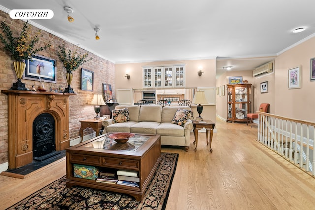 living room featuring a wall mounted AC, light hardwood / wood-style floors, brick wall, a fireplace, and ornamental molding