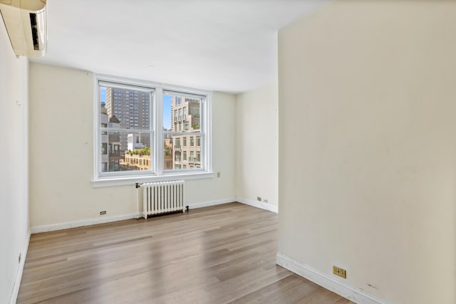 empty room featuring baseboards, radiator heating unit, a view of city, and light wood-style floors