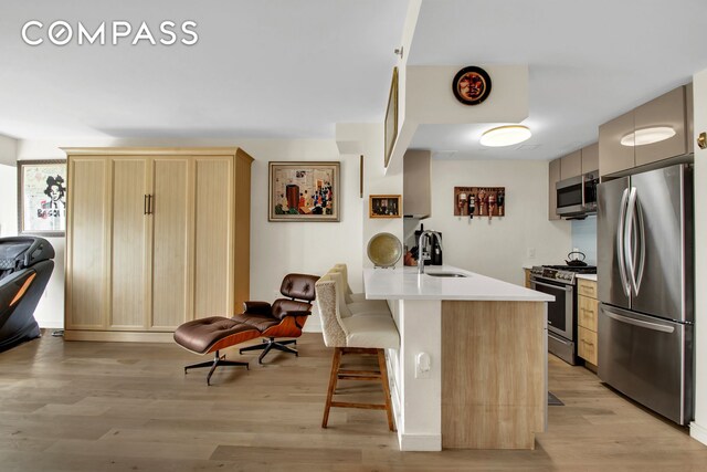 kitchen with sink, a breakfast bar area, light brown cabinets, stainless steel appliances, and light hardwood / wood-style floors