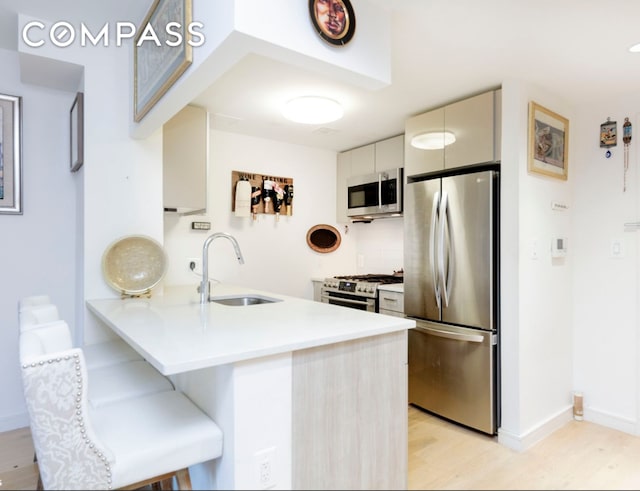 kitchen with a breakfast bar, a peninsula, a sink, stainless steel appliances, and light countertops