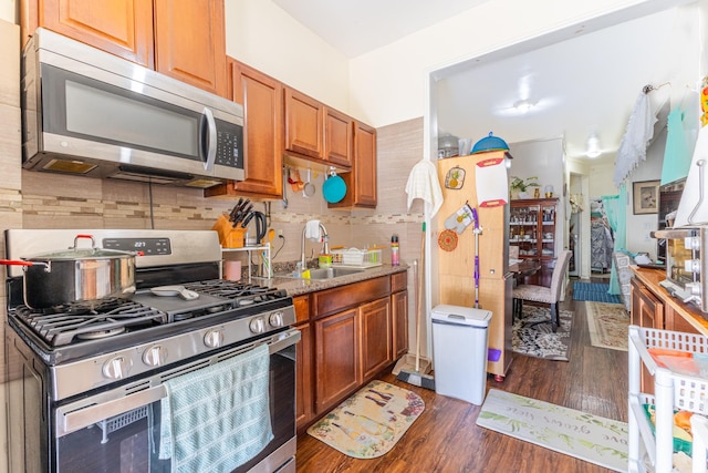 kitchen featuring a sink, appliances with stainless steel finishes, decorative backsplash, brown cabinets, and dark wood finished floors