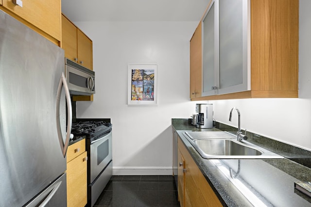 kitchen featuring baseboards, dark countertops, stainless steel appliances, dark tile patterned floors, and a sink