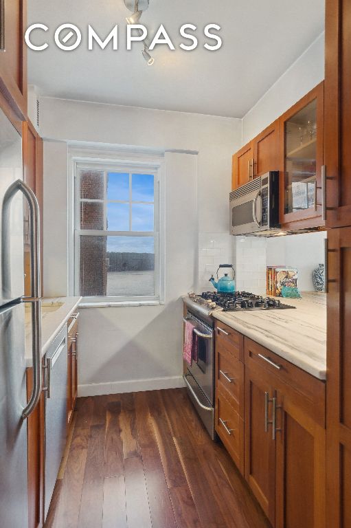 kitchen with tasteful backsplash, appliances with stainless steel finishes, dark hardwood / wood-style floors, and light stone counters