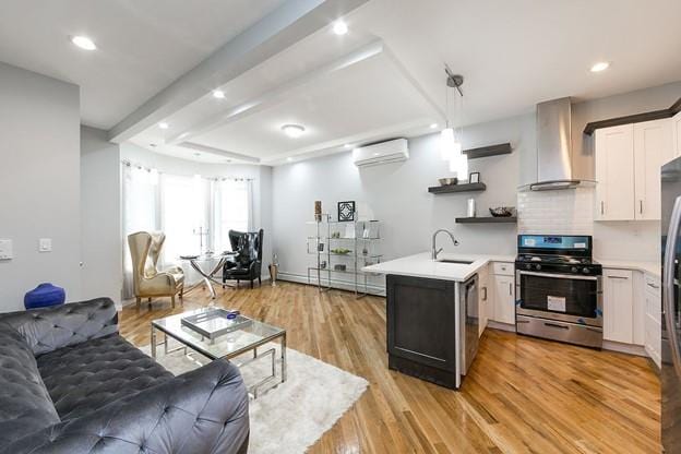 kitchen with a wall unit AC, a peninsula, a sink, stainless steel gas stove, and wall chimney exhaust hood