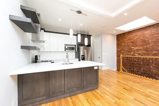 kitchen with a peninsula, appliances with stainless steel finishes, brick wall, and light countertops