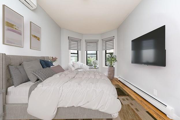 bedroom with a baseboard heating unit, a wall mounted air conditioner, and wood finished floors