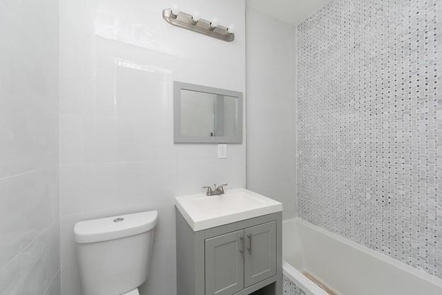 bathroom with toilet, bathing tub / shower combination, tile walls, and vanity