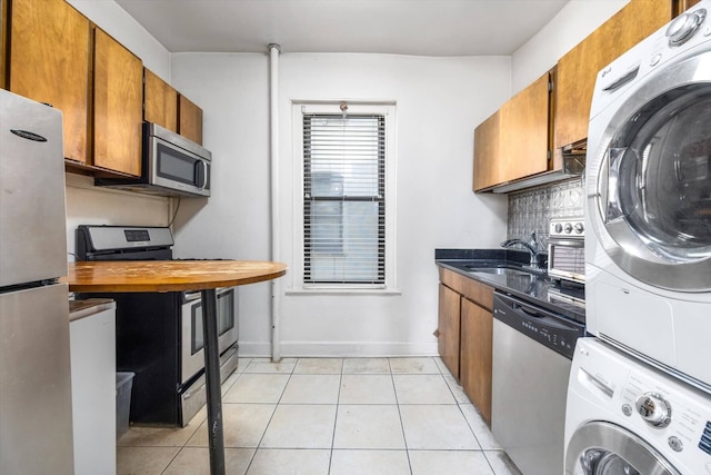 kitchen with appliances with stainless steel finishes, brown cabinets, backsplash, a sink, and stacked washing maching and dryer