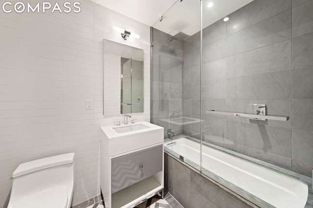 full bathroom featuring tile walls, vanity, tiled shower / bath combo, and toilet