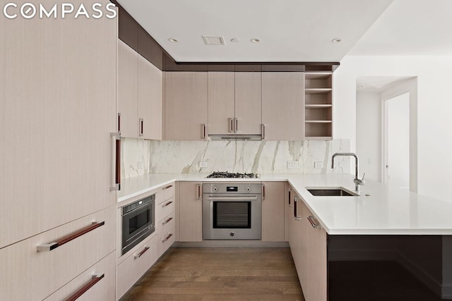 kitchen with sink, dark wood-type flooring, backsplash, stainless steel appliances, and kitchen peninsula