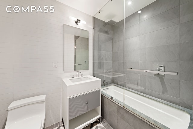 bathroom with toilet, tiled shower / bath combo, vanity, and tile walls