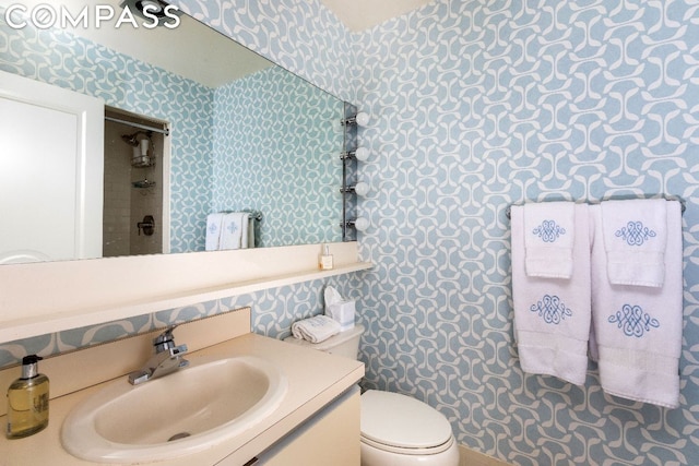 full bath with toilet, wallpapered walls, vanity, and walk in shower