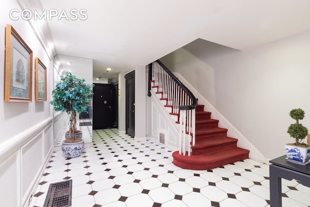 entrance foyer with visible vents, light floors, stairway, and a decorative wall