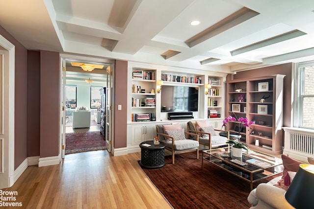 living room featuring built in shelves, coffered ceiling, beam ceiling, and light hardwood / wood-style flooring