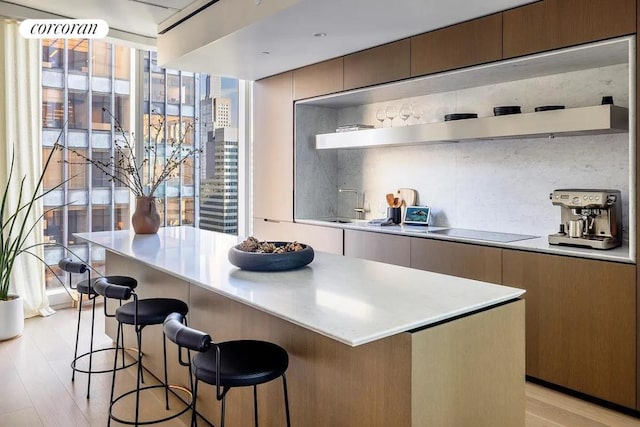 kitchen with sink, a kitchen island, black electric stovetop, light hardwood / wood-style floors, and backsplash