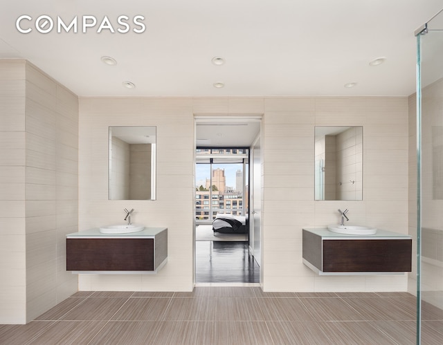 full bath with a sink, two vanities, and tile walls