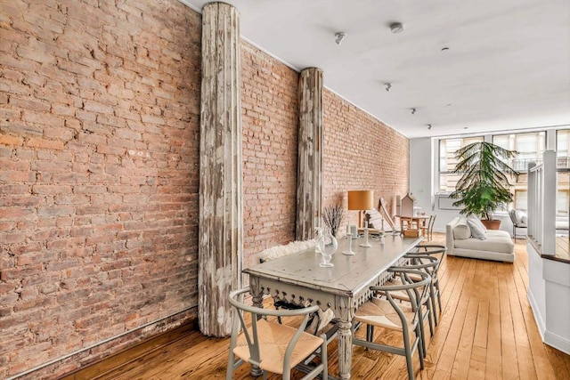 dining space with brick wall and light wood-type flooring